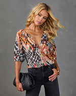Woman wearing abstract ikat print V-neck blouse with puff sleeves, dark jeans, holding black woven clutch bag