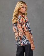 Woman modeling abstract ikat-print blouse with elbow sleeves in rust, navy, and cream tones, paired with dark jeans