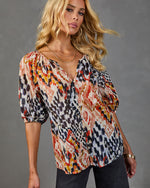 Woman wearing multicolor ikat print button-front blouse with puff sleeves, paired with dark jeans and gold jewelry