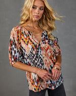 Woman wearing multicolor ikat print button-front blouse with 3/4 sleeves, styled with gold jewelry and dark jeans