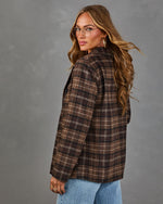 Woman in brown plaid wool blazer, light-wash jeans, wire-rim glasses and gold hoop earrings, looking back over her shoulder