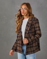 Woman wearing a brown plaid double-breasted blazer over a white tee, light-wash jeans, and clear aviator glasses