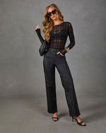 Woman in sheer black plaid mesh bodysuit, coated high-waisted wide-leg jeans, black heels, woven handbag and gold bangles