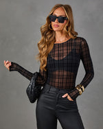 Woman wearing a black sheer plaid mesh long-sleeve bodysuit with coated skinny jeans, gold bangles, and a woven black clutch