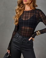 Sheer black plaid flocked mesh long-sleeve bodysuit styled with coated high-waisted black pants and chunky gold bracelets