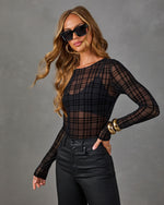 Woman wearing a sheer black plaid flocked mesh long-sleeve bodysuit with coated black pants, gold bangles and square sunglasses