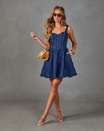 Woman wearing dark blue denim mini dress with corset bodice, flared skirt, styled with tan bag and clear heels