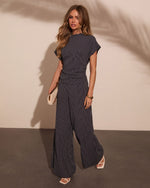Woman wearing navy pinstripe wide-leg pants and matching cap-sleeve top with white heels and cream clutch bag