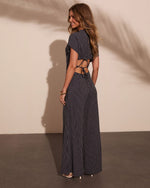 Navy pinstripe open-back maxi jumpsuit with short sleeves, lace-up waist cutout, worn with nude heels and gold bangles