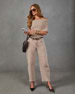 A woman modeling a beige off-the-shoulder knit top, beige wide-leg cropped jeans, and black pointed-toe heels against a gray studio backdrop.