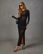 Woman in black sheer plaid long-sleeve maxi dress with side slit, black heels, sunglasses, and woven clutch against gray backdrop