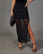 Black sheer plaid maxi skirt with high side slit, styled with black strappy heeled sandals and a woven leather handbag