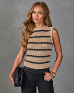 Woman wearing tan and black striped open-knit crochet sweater vest with black jeans, gold jewelry, and black woven clutch