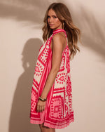 Woman modeling pink geometric print halter mini dress with pleated hem, gold bangle bracelet, and hoop earrings
