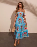Woman wearing blue floral off-shoulder midi dress with red flowers, straw bag, and tan flip flops in summer style