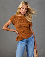 Woman wearing rust brown ribbed knit peplum sweater top with blue jeans, gold hoop earrings, and woven bag