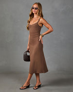 Brown knit midi dress with spaghetti straps on woman styled with gold cuff bracelet, woven bag, and black sandals