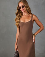 Woman wearing brown knit midi slip dress with V-neckline, styled with gold cuff bracelet, tortoise sunglasses, and woven clutch