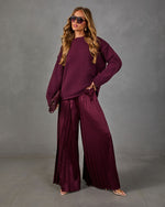Woman in oversized burgundy knit sweater and wide-leg pleated satin pants with maroon clutch and clear-strap heels