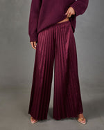 Burgundy satin pleated wide-leg pants styled with an oversized plum knit sweater and clear strappy heels