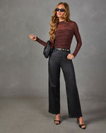A woman modeling a dark brown long-sleeve ribbed top and black wide-leg jeans against a textured gray studio background.