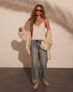 Woman wearing white lace cami, beige oversized cardigan, light wash wide-leg jeans, and strappy sandals with tinted sunglasses