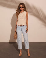 Woman wearing cream knit sleeveless top, light wash cropped jeans, brown belt, clear heeled sandals, holding woven clutch bag.