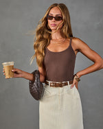 Woman wearing brown ribbed tank bodysuit, cream corduroy midi skirt, brown woven bag, holding iced coffee, brown belt