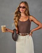 Woman wearing brown ribbed tank bodysuit, cream corduroy midi skirt, brown woven bag, holding iced coffee, brown belt