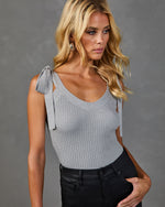 Silver ribbed knit bodysuit with shoulder tie straps, worn with black high-waist jeans on blonde female model