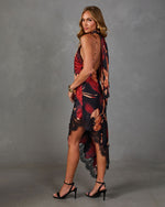 Woman in a red and black floral satin halter midi dress with open back, black lace asymmetric hem, and black strappy heels