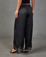 Black satin wide-leg pants with lace hem trim, elastic waist, paired with black kitten heels, back view