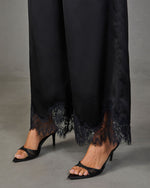 Black satin wide-leg pants with floral lace hem trim, styled with black pointed-toe stiletto mule heels