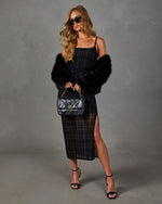 Woman in black plaid sheer midi dress with side slit, faux fur jacket, quilted chain handbag, sunglasses and strappy heels