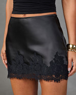 Black satin mini skirt with lace trim hem, worn with black crop top and gold cuff bracelet