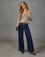 Woman wearing wide-leg dark wash jeans, beige cable-knit cardigan, brown heeled boots, glasses, and crossbody bag