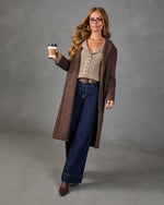 Woman in brown long wool coat, beige ribbed sweater, wide-leg dark jeans, brown ankle boots, holding coffee cup