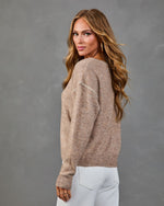 Woman modeling taupe knit sweater with contrast stitching detail and ribbed cuffs, paired with white jeans