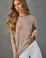 Woman wearing oversized taupe knit sweater with stitch detail neckline and white jeans, long wavy blonde hair