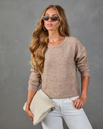 Woman wearing taupe knit sweater with stitch detail and white jeans, holding cream woven leather clutch, tortoiseshell sunglasses