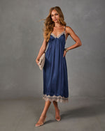 Navy satin midi slip dress with beige lace trim, styled with clear heels, a woven clutch and gold cuff bracelet