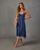 Navy satin midi slip dress with beige lace trim, styled with clear heels, a woven clutch and gold cuff bracelet
