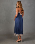 Woman in a navy satin midi slip dress with cream lace trim and open V-back, styled with nude strappy heeled sandals