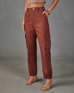 Women's rust brown high-waist cargo jogger pants with side pockets, button closure, elastic ankles, styled with heels