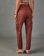 Women's rust brown cargo jogger pants with side pockets, elastic ankles, worn with nude heels, back view