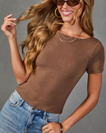 Woman wearing brown fitted short-sleeve knit top with blue jeans, layered gold necklaces, hoop earrings, and tortoise sunglasses