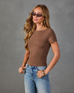 Woman wearing fitted brown short-sleeve crop top with light wash jeans, gold hoop earrings, layered necklaces, and cat-eye sunglasses