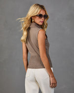 Woman wearing sleeveless brown turtleneck knit sweater vest, white jeans, tortoise sunglasses, gold hoop earrings, back view