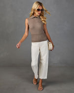 Woman wearing taupe sleeveless collared knit top, white wide-leg jeans, strappy nude heels, and oversized sunglasses