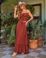 Woman wearing rust brown boho crop top and maxi skirt set with cowboy hat, sunglasses, and tan ankle boots outdoors